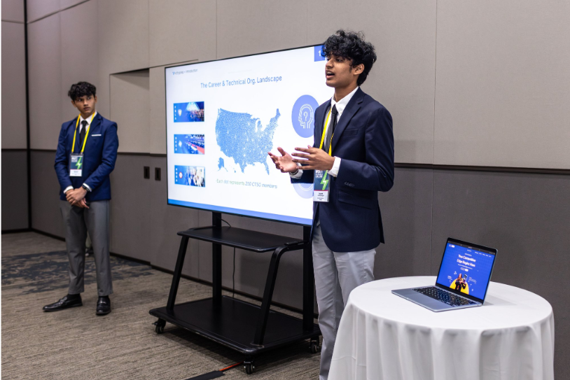 Two students present next to a large monitor